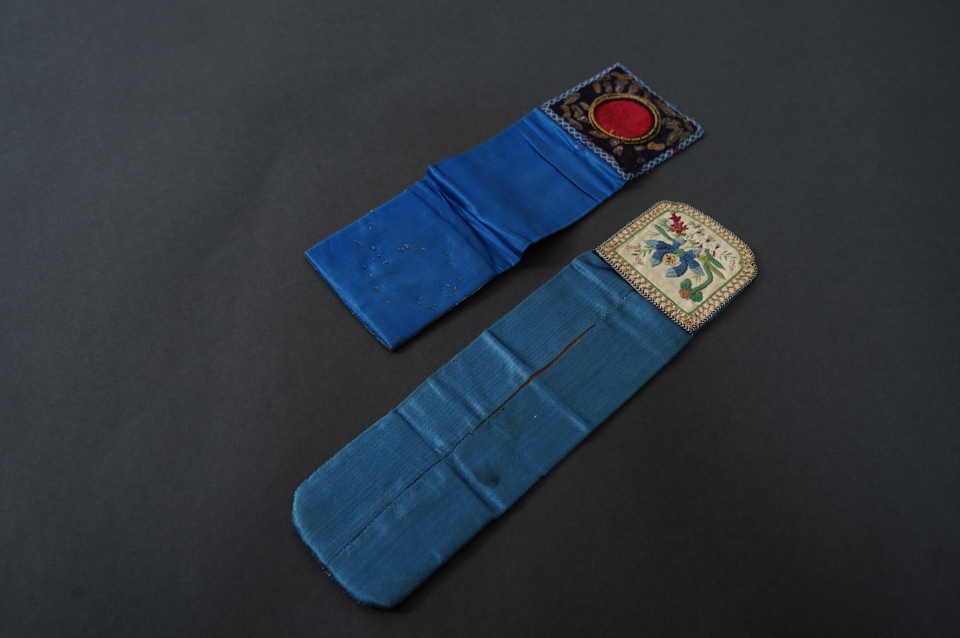 Two Chinese late Qing Dynesty coloured silk and gold thread embroidered belt purses, or ‘hebao’, for carrying coins, seals and fragrant herbs etc. One - 19cm long,in cream silk, with the embroidered words: “It’s music is
